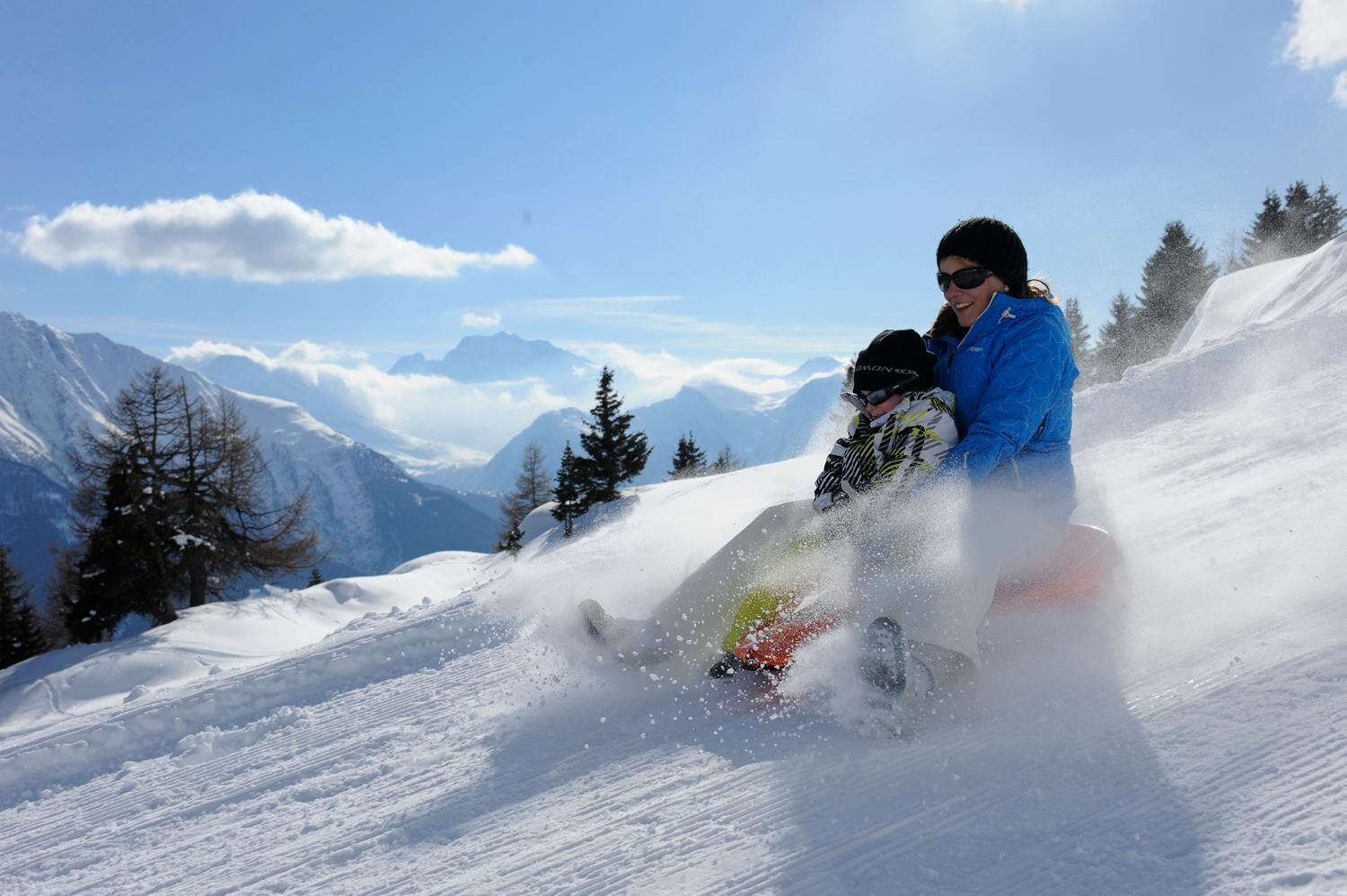 A person snowboarding down a snowy slope with mountains in the background.