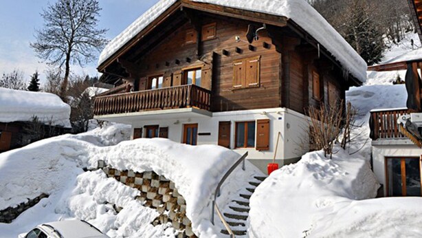 A wooden chalet with a balcony, surrounded by snow-covered ground and trees. - Stachelbeere UG (Fiesch)