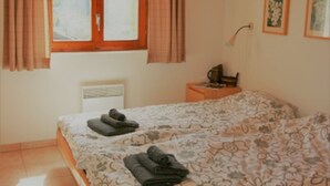 A bedroom with a bed, a nightstand, a window with curtains, and a wall-mounted lamp. - Stachelbeere UG (Fiesch)