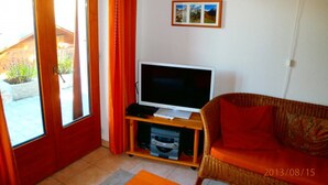 A living room with a television on a stand, a wicker sofa, and a small table. - Stachelbeere UG (Fiesch)