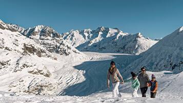 Eine Familie wandert auf einem verschneiten Bergpfad, im Hintergrund Gletscher und Berge.