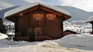 Une cabane en bois, avec un toit enneigé, une porte en bois et des fenêtres équipées de volets.