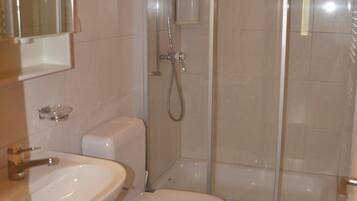 Un baño con inodoro, lavamanos y ducha con mampara de vidrio.