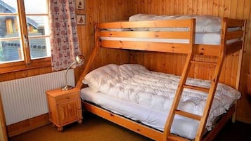 Una cama individual sobre otra con estructura de madera, una mesita de noche con lámpara y una ventana con cortinas.