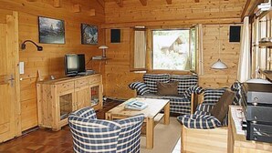 Interior d'una cabana acollidora amb parets de fusta, una televisió, una llar de foc i una zona de menjador.