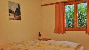 Un dormitori amb un llit, una finestra amb cortines, una tauleta de nit i un quadre a la paret.