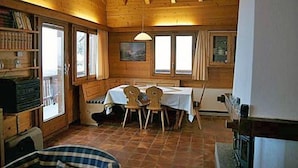 Interior d'una cabana de fusta amb zona de menjador, una llar de foc i una prestatgeria.