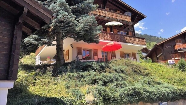 A traditional chalet with a wooden balcony, a large tree in front, and a red umbrella. - Wasserhügeli (Fiesch)