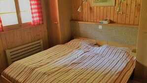 A wooden room with a bed, a window with red curtains, and a painting on the wall. - Wasserhügeli (Fiesch)