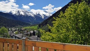 A mountain landscape with snow-capped peaks, a valley with houses, and a wooden fence in the foreground.