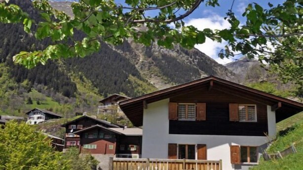 A two-story chalet with a balcony, surrounded by a mountainous landscape.