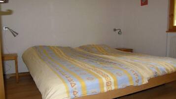 Una cama individual con cubrecama estampado en una habitación con suelo de madera y paredes blancas.