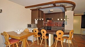 A compact kitchen with a dining area, featuring a wooden table and chairs, a microwave, and a stove. - Wolf (Fieschertal)