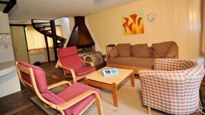 A living room with a fireplace, a checkered sofa, a red armchair, and a wooden coffee table. - Wolf (Fieschertal)