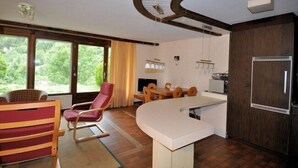 A modern kitchen with a built-in refrigerator, wooden cabinets, and a dining area with a curved white table and wooden chairs. - Wolf (Fieschertal)