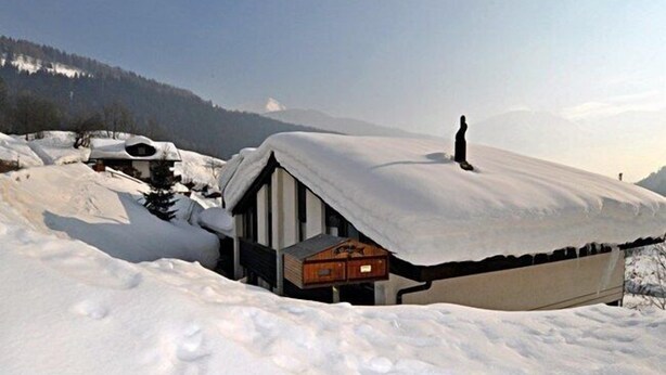 A snow-covered chalet with a wooden exterior and a sloped roof, surrounded by snow and mountains. - Wolf (Fieschertal)