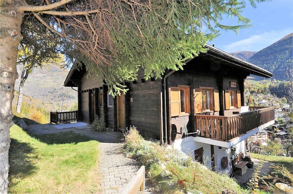 A wooden cabin with a balcony, surrounded by trees and a mountainous landscape. - Uf der Egga 419 (Fiesch)