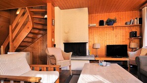 A cozy cabin interior with a wooden staircase, a fireplace, a television, and a sofa. - Uf der Egga 419 (Fiesch)