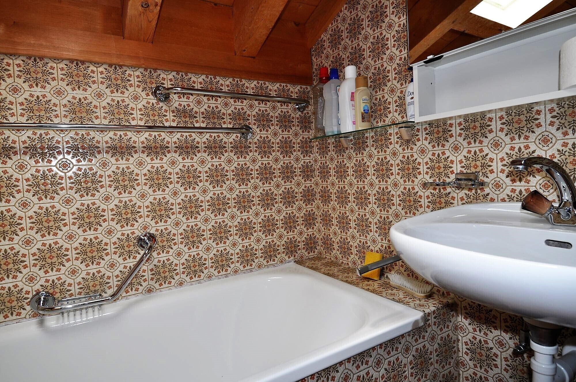 A bathroom with a white bathtub, a sink, and a shower. There are toiletries on a shelf above the sink.