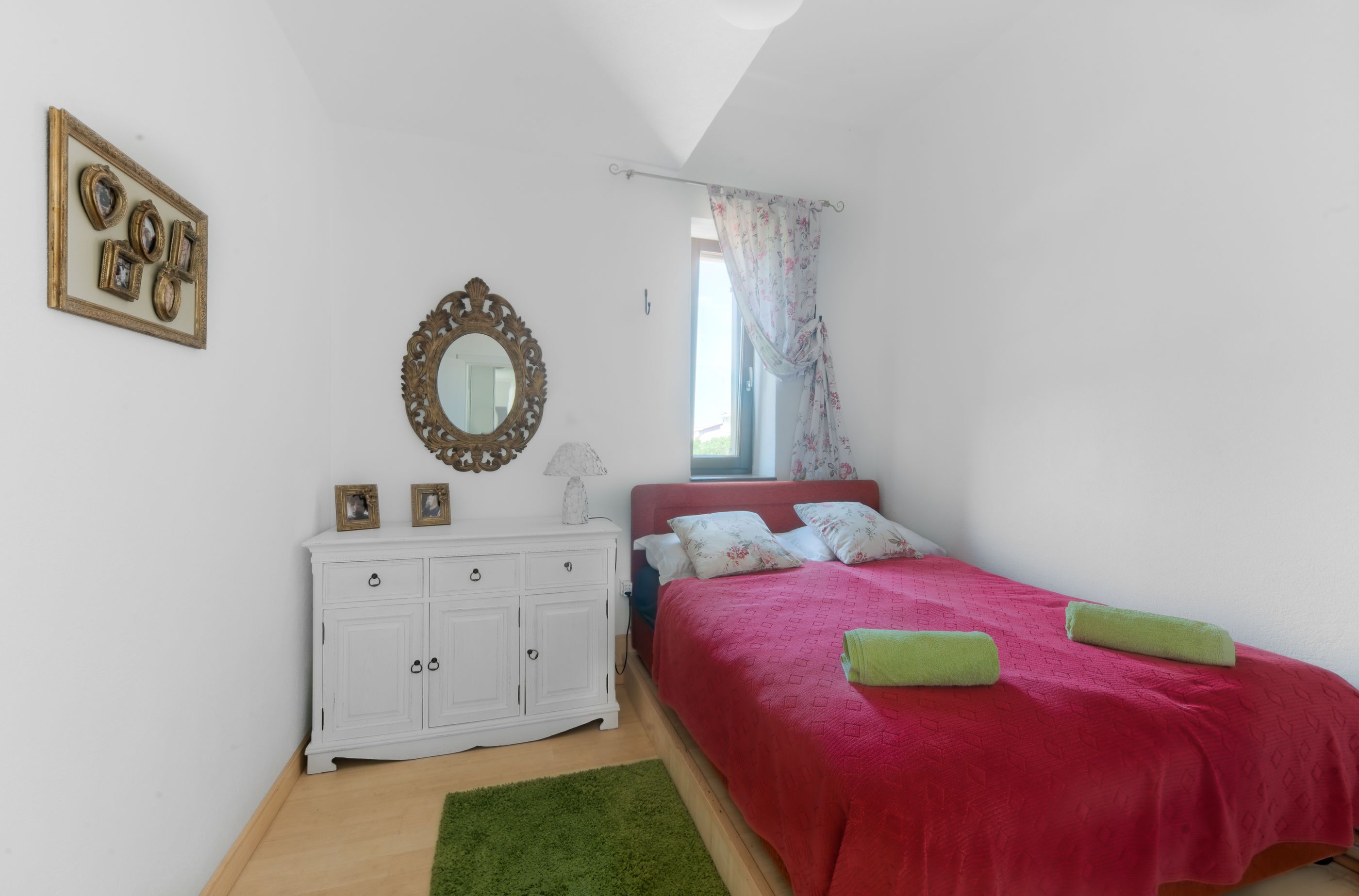 Un dormitorio con cama, cómoda, espejo y ventana con cortinas.