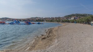 A beach with a sandy shore and a water body. There are buildings in the background.