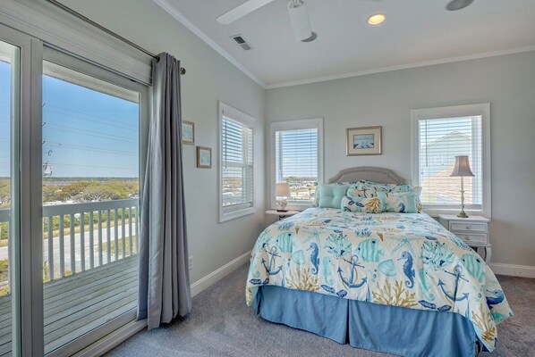 A bedroom with a large bed, two bedside tables, a window with blinds, and a view of the outdoors. - 3952 Island Drive- Oceanfront Home with views and private beach access- Adjoining Side is Availab... (North Topsail Beach)