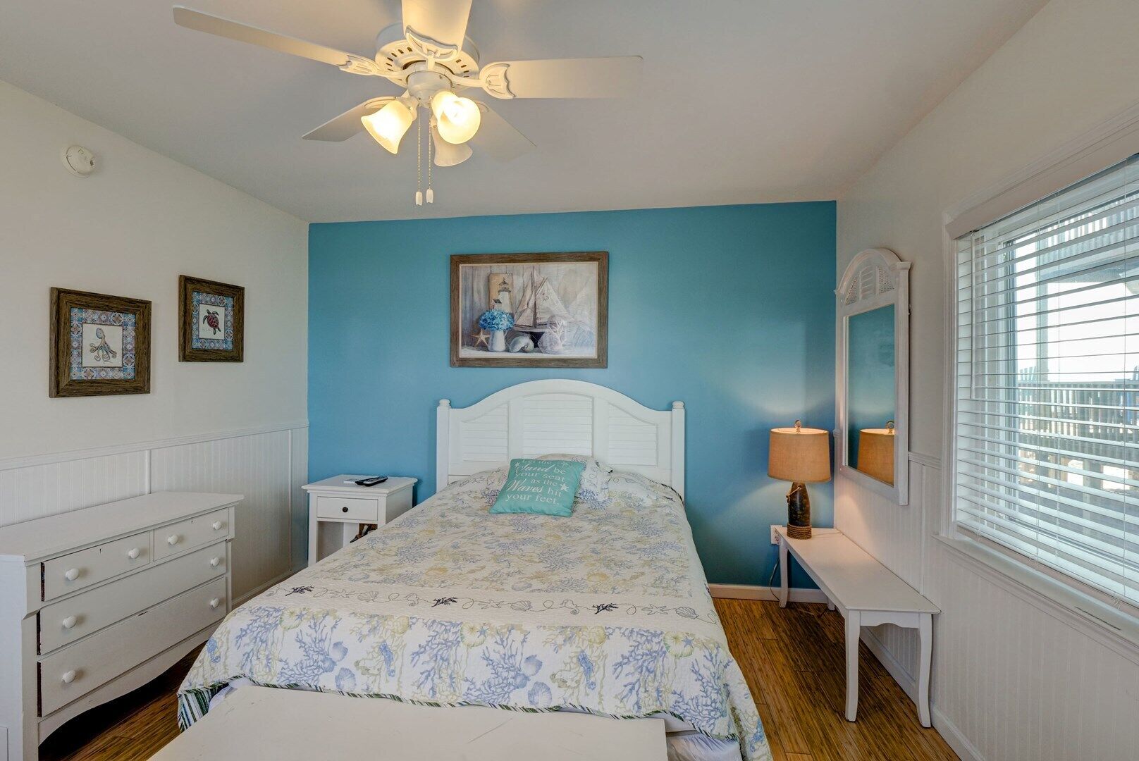 A bedroom with a bed, a nightstand, a dresser, a ceiling fan, a painting, and a window with blinds.