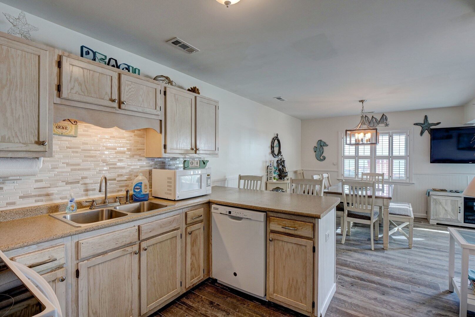A kitchen with wooden cabinets, a microwave, and a sink. There is a dining area with a table and chairs.