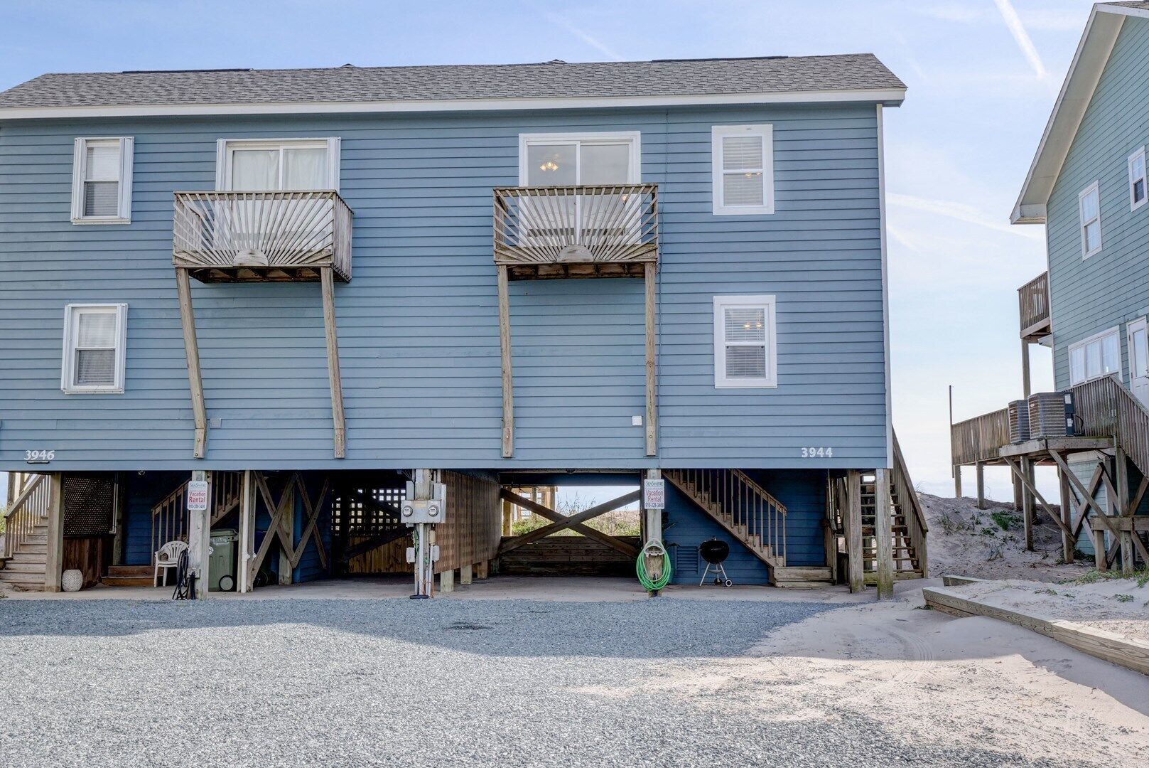 A two-story building with a balcony on the second floor, a wooden deck on the ground floor, and a gravel driveway.