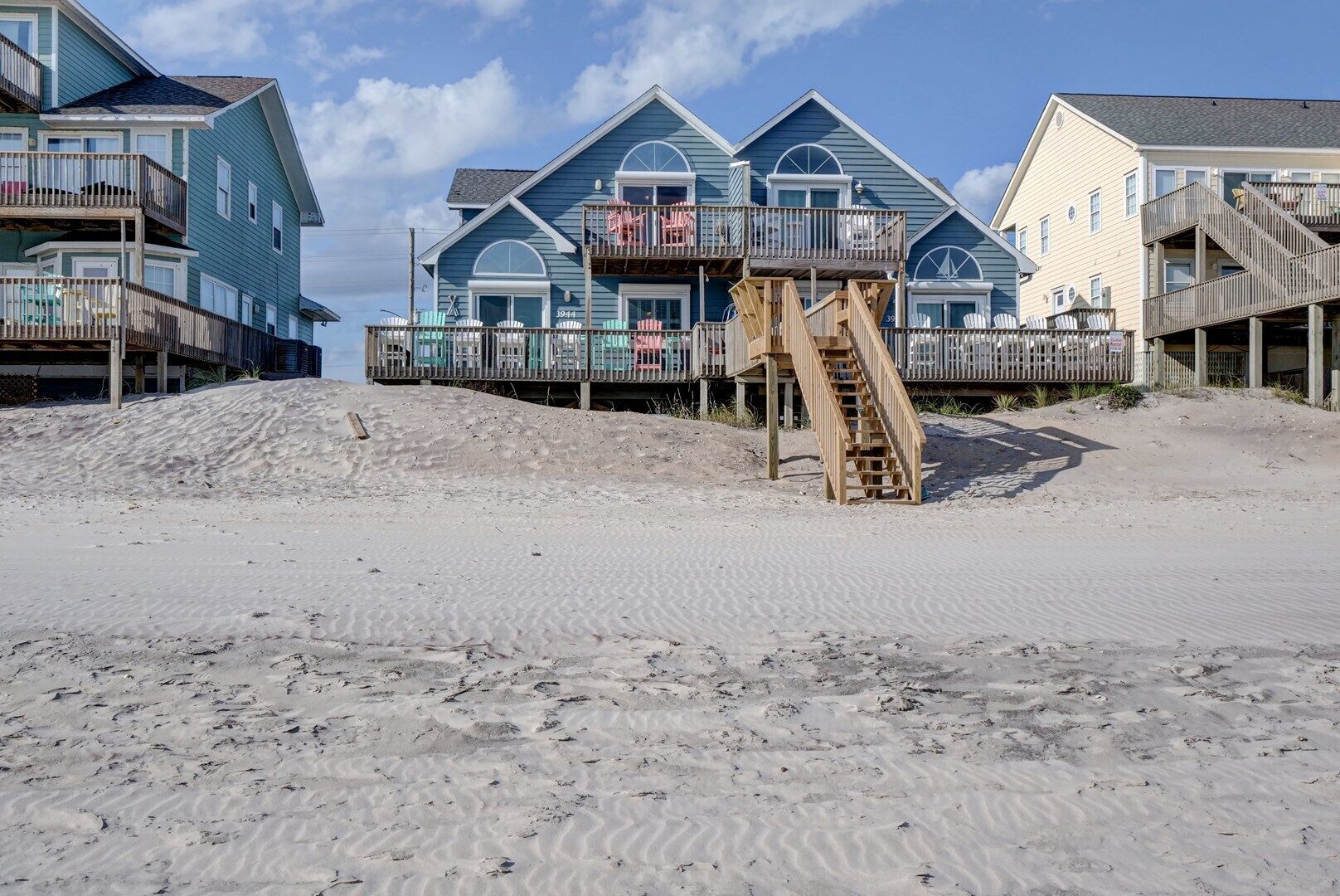 Un hotel frente a la playa con varios balcones, una escalera de madera que baja a la arena y una orilla arenosa.