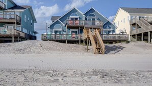 Un hotel frente a la playa con varios balcones, una escalera de madera que baja a la arena y una orilla arenosa.