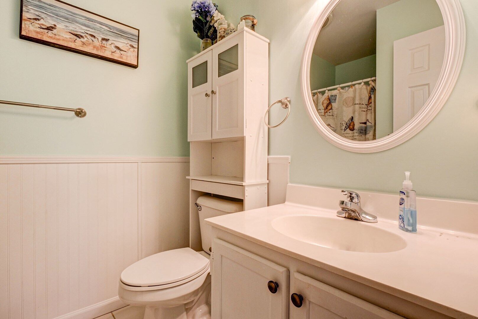 Ein Badezimmer mit einer weißen Toilette, einem Waschbecken mit Spiegel darüber und einem Schrank mit einer dekorativen Vase.