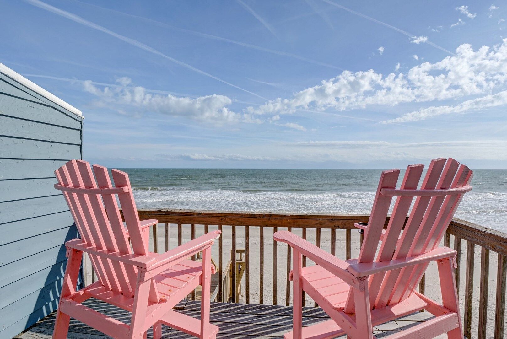 Twee roze Adirondack stoelen op een houten terras met uitzicht op de oceaan.