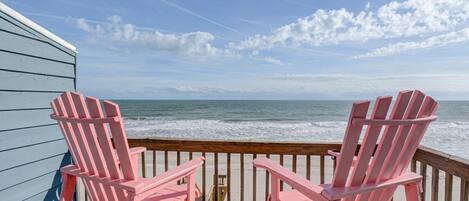 Twee roze Adirondack stoelen op een houten terras met uitzicht op de oceaan.