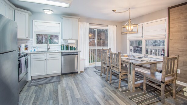 Une cuisine moderne avec des meubles blancs, un réfrigérateur en acier inoxydable et une table à manger en bois, assortie de chaises.
