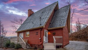 Une maison en bois rouge, avec un toit à forte pente, un porche à l’avant et le numéro « 289 » bien visible sur le côté.