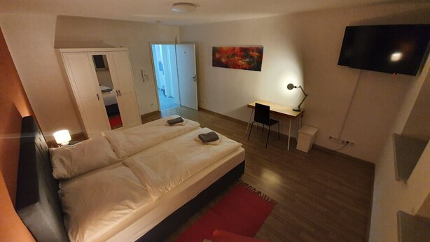 A bedroom with a bed, a desk, a TV, and a door leading to another room. - White Pearl Hostel 2 (Nuremberg)
