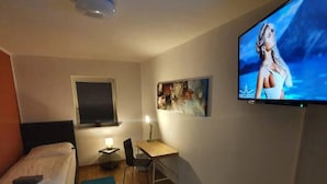 A small, well-lit room with a bed, a desk, a chair, a TV, and a window with blinds. - White Pearl Hostel 2 (Nuremberg)
