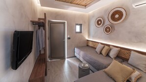 A modern room with a flat-screen TV, a sofa with cushions, a small table, and a wall-mounted shelf. - Oasis Hotel Prasonisi (Rhodes)