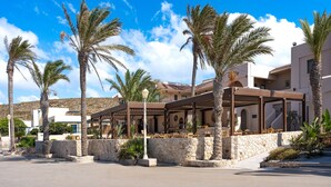 A hotel with outdoor seating, palm trees, and a stone wall. - Oasis Hotel Prasonisi (Rhodes)