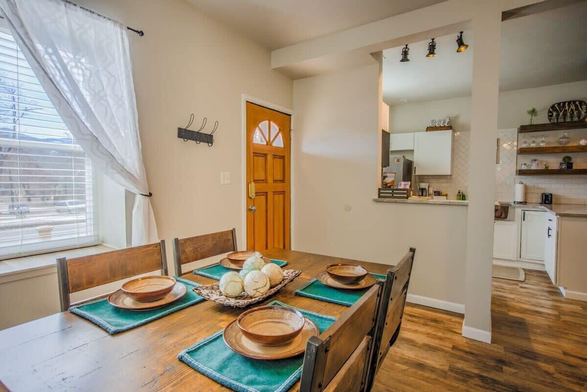 A dining area with a wooden table set for six, a kitchen in the background, and a door with a window.