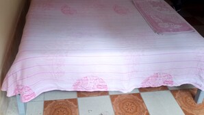 A bed with a pink bedspread and two pillows, a small table, and a chair in a room with yellow walls. - Orchards Lodge (Naivasha)