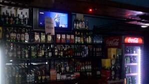A bar with shelves of liquor bottles and a Coca-Cola refrigerator. - Orchards Lodge (Naivasha)