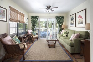 A living room with a television, a green sofa, a wicker chair, and a glass coffee table. - Home away from home! (Key West)