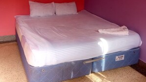Een enkel bed met klamboe, witte beddengoed en een blauwe koffer onder het bed.
