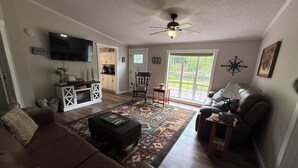 A living room with a brown sofa, a television, a ceiling fan, and a view of the outdoors through a sliding glass door.