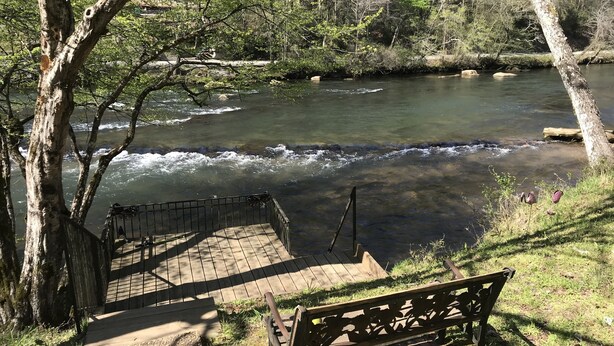 A wooden bench overlooking a river with a bridge and steps leading down to the water.