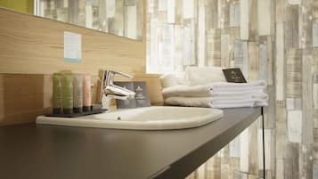 A modern bathroom with a large mirror, a white sink, and neatly stacked towels.