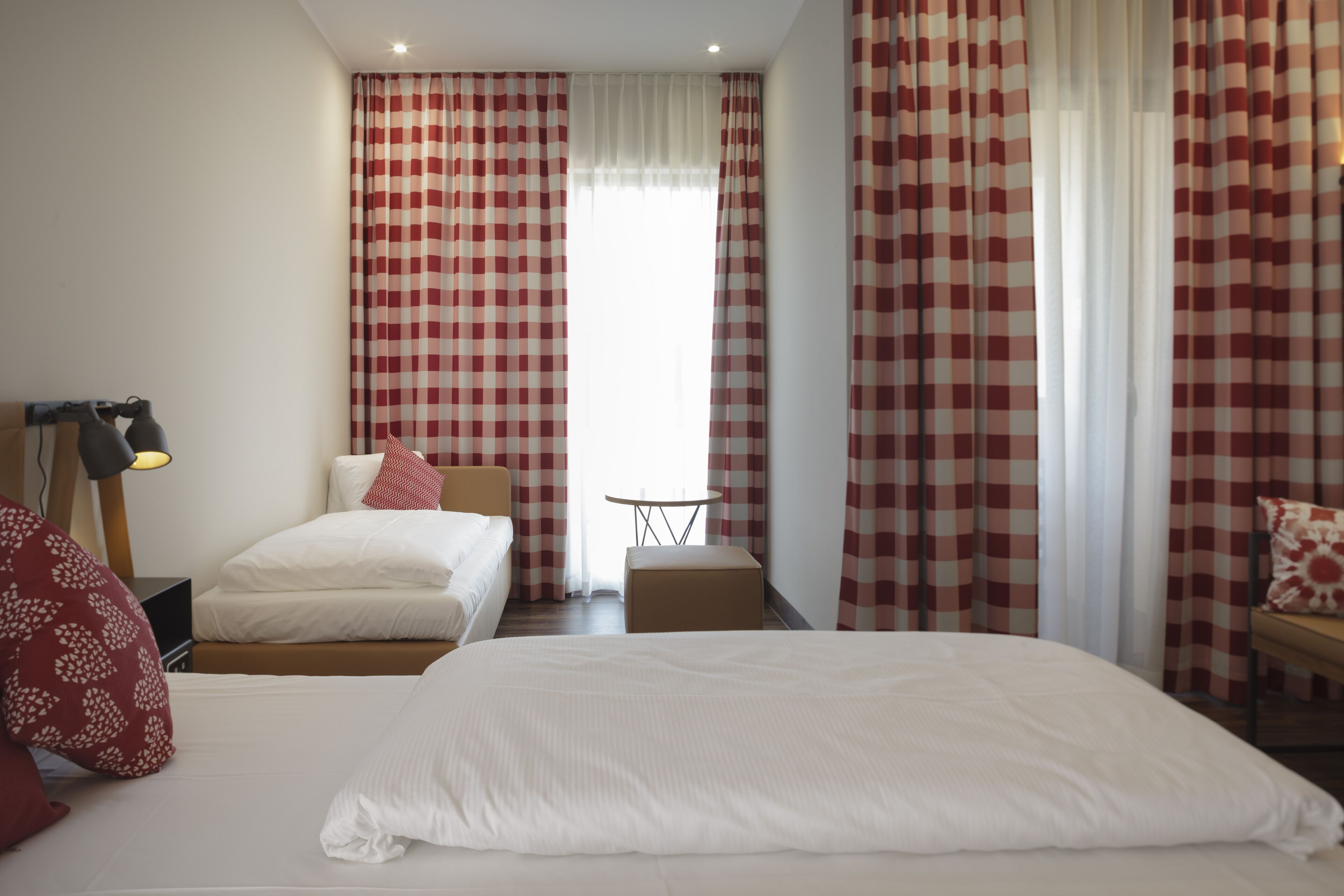 Une chambre d’hôtel avec un grand lit, une table de chevet, une lampe, une petite table et des rideaux à carreaux.