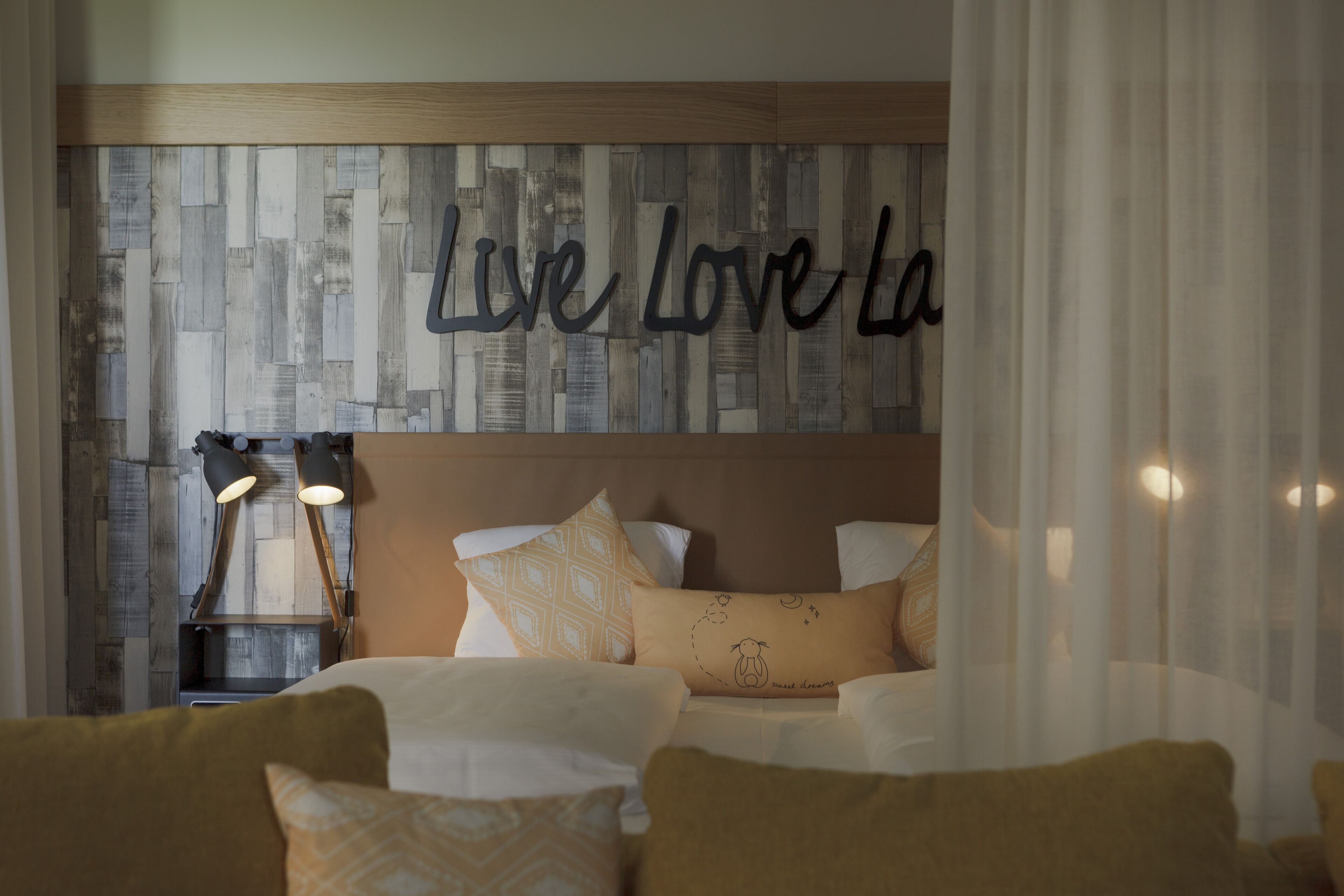 A bedroom with a bed, pillows, a wall with 'Live Love LA' text, and a nightstand with lamps.